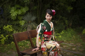 緑の中椅子に座った振袖を着た二十歳