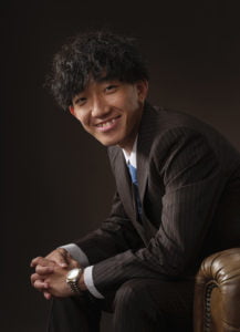 横向きに座って正面を向いたスーツを着た成人男性