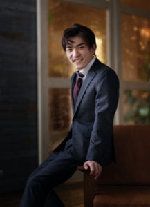 椅子の肘掛けに腰掛けたスーツを着た男性