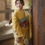 窓辺で壁に手をつき振り返る振袖を着た二十歳